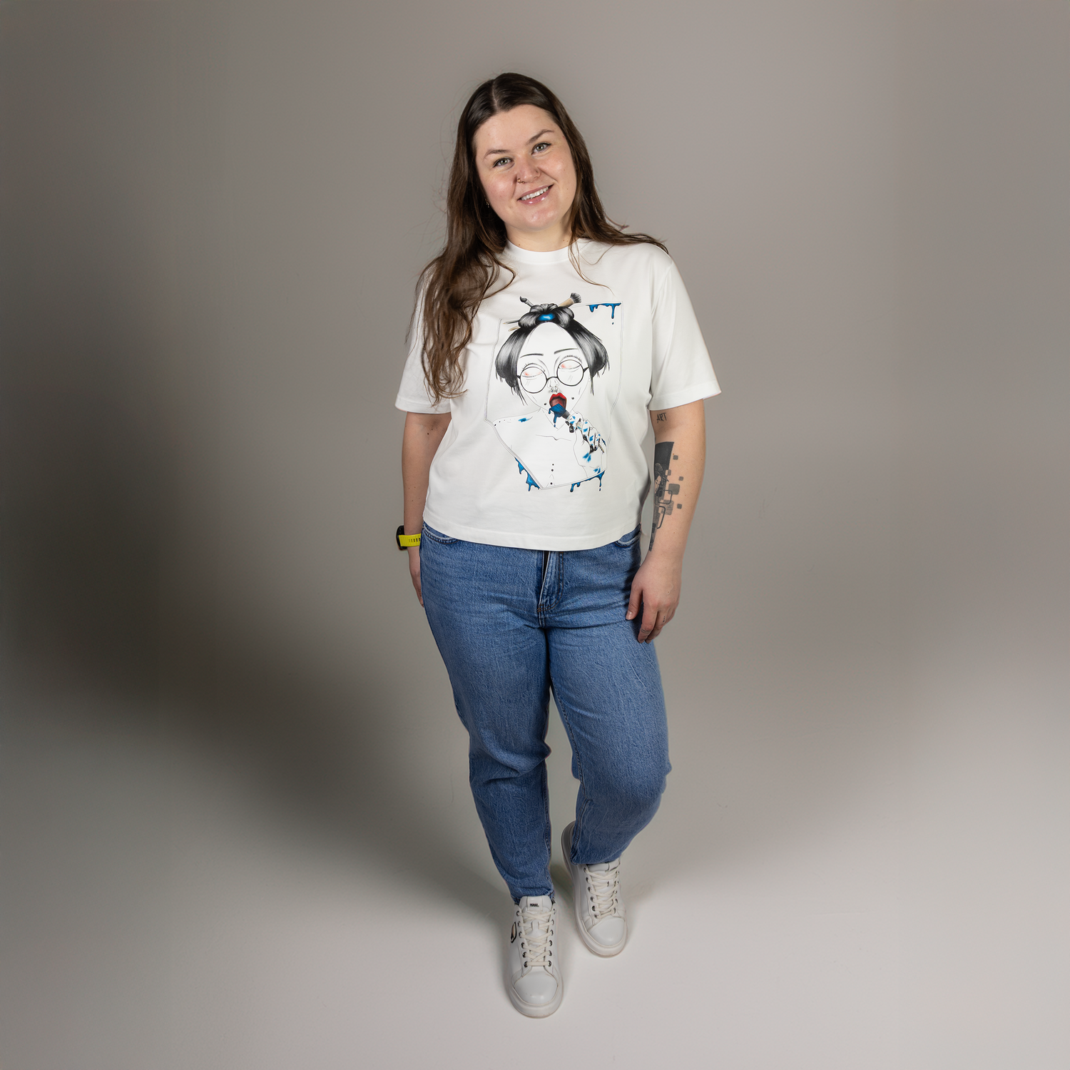 Person wearing a white t-shirt with a graphic design and blue jeans on a gray background