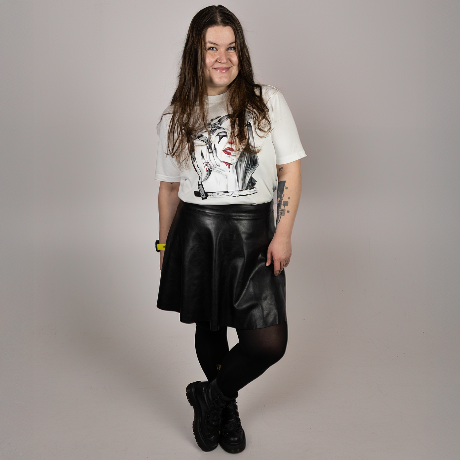 Person wearing a white graphic designed t-shirt, black leather skirt, and black boots on a plain background