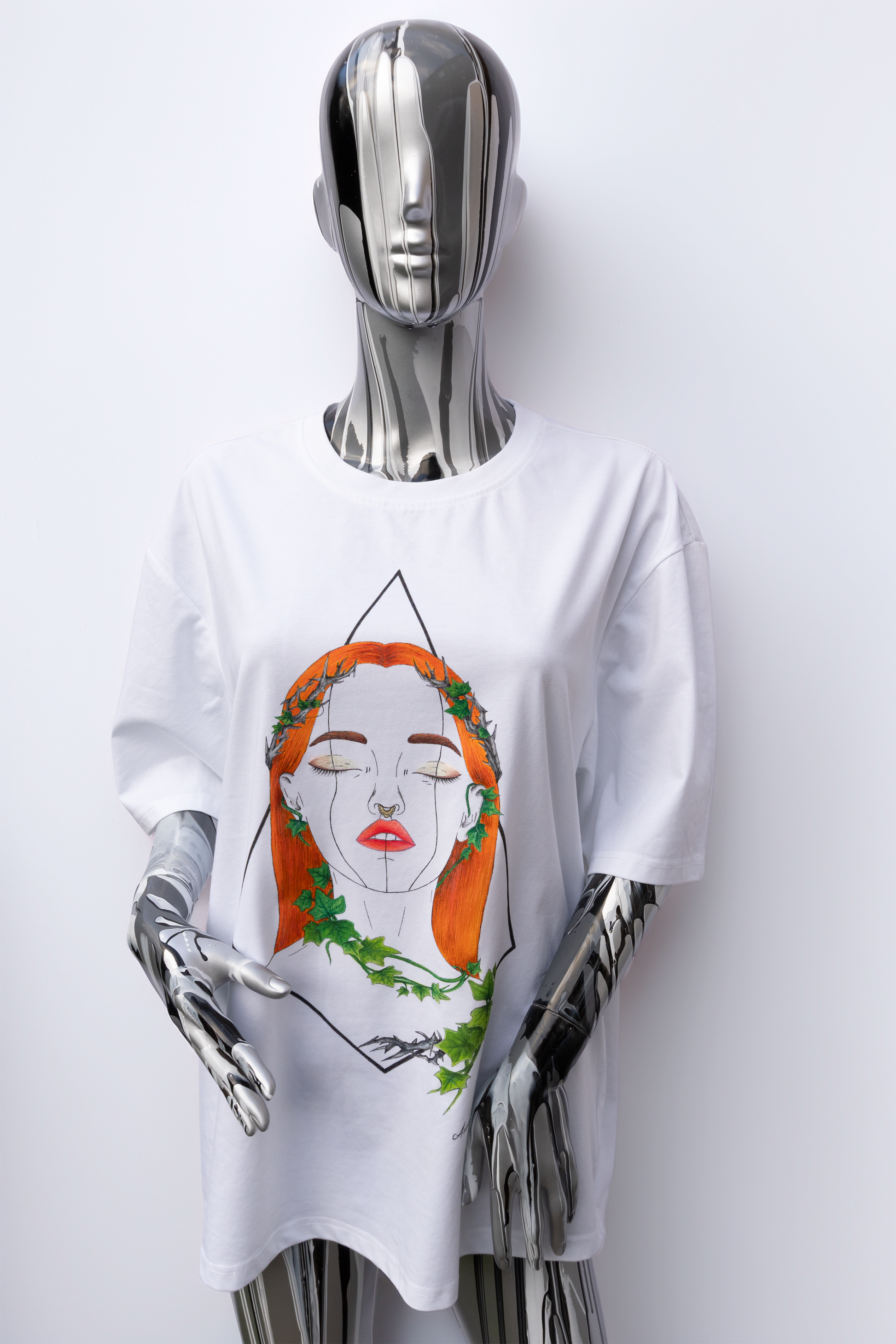 Female mannequin wearing a white t-shirt with a graphic design on a plain background. The design is hand painted and shows a girl with round glasses, blue paint dripping and a brush.