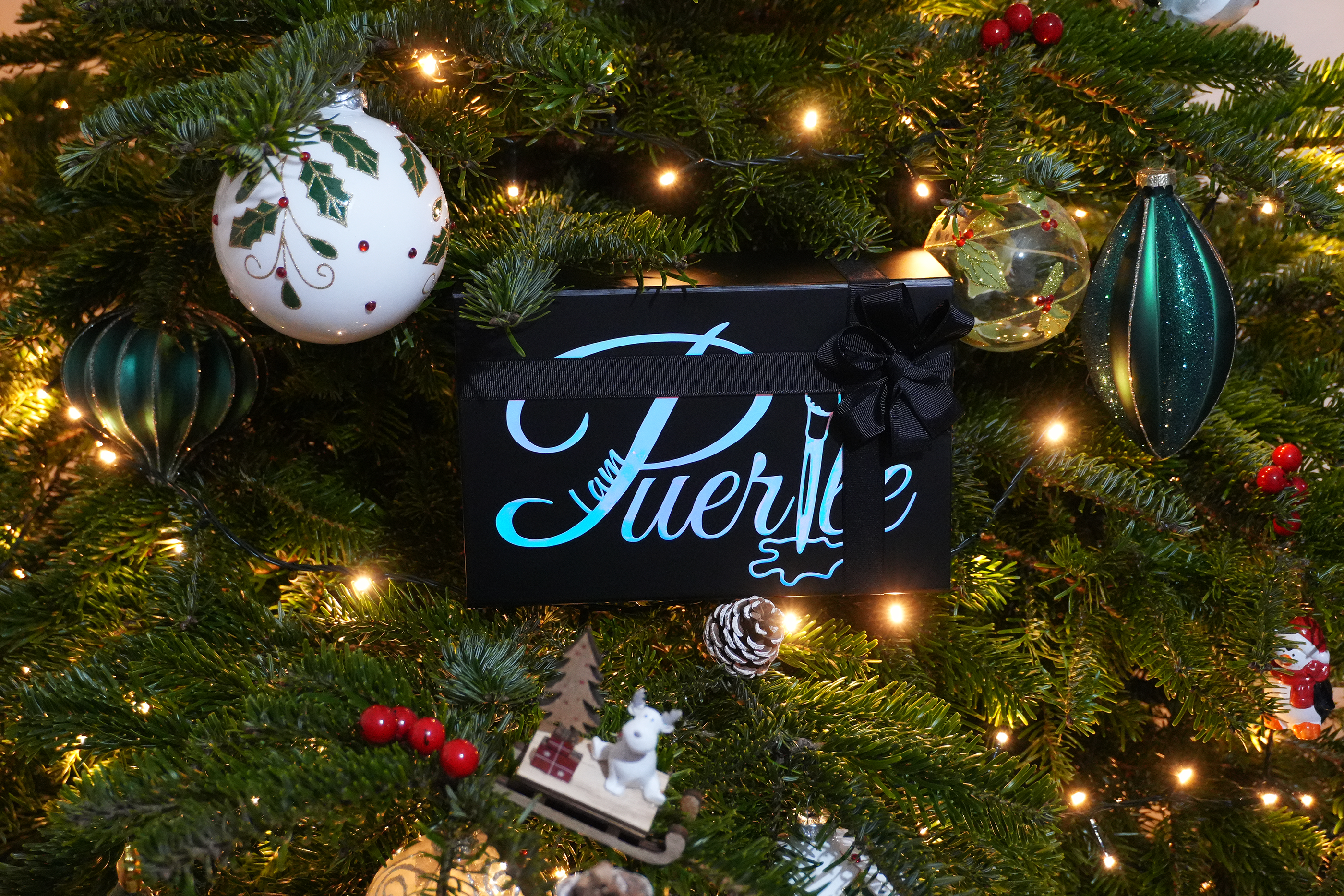 Decorative box with 'I am Puerile' logo on a Christmas tree with ornaments and lights.