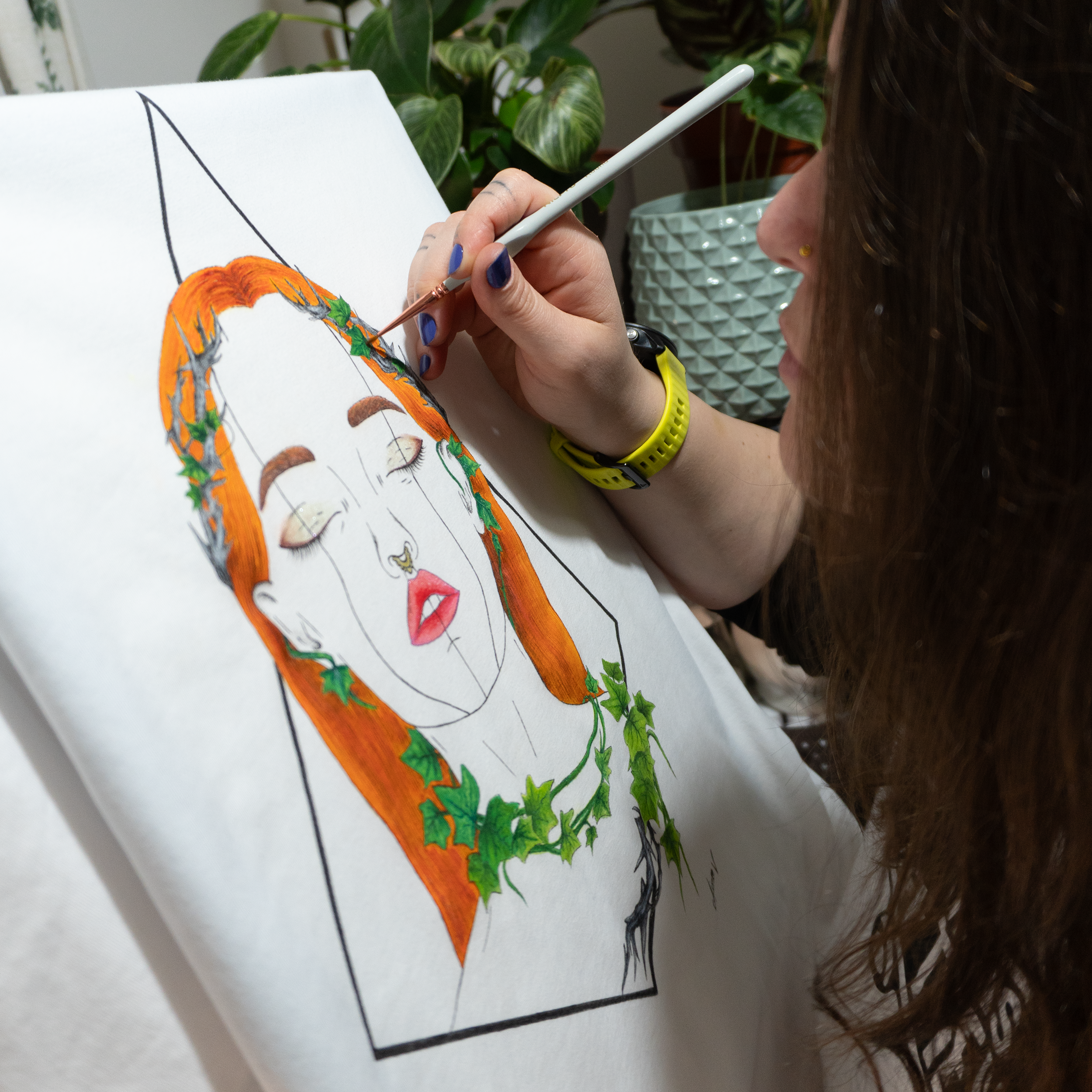 Person painting a woman with orange hair and green leaves on a white cotton t-shirt.