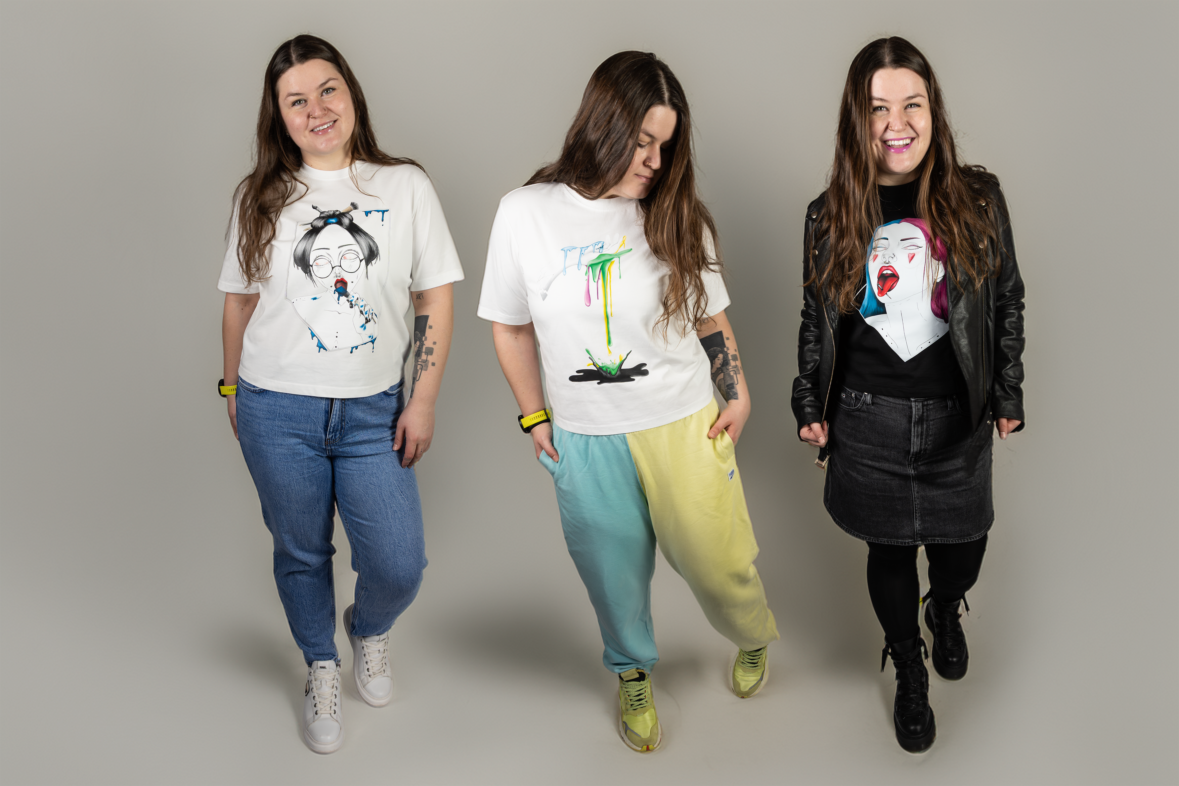 Three women wearing hand drawn graphic t-shirts on a plain background